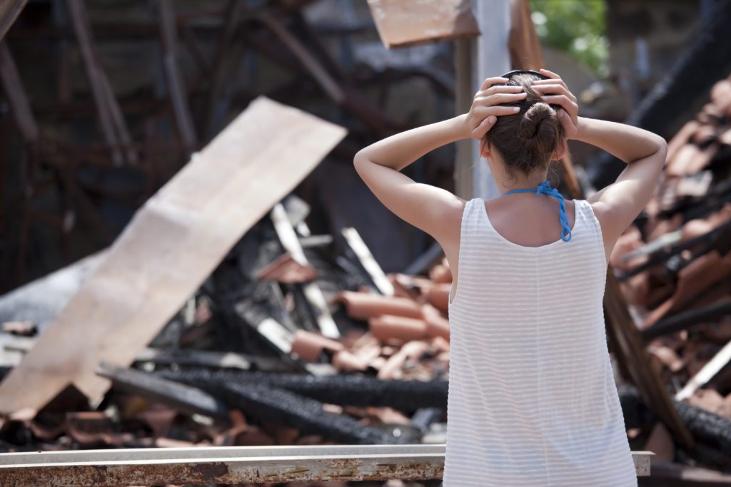 Woman,Standing,In,Front,Of,Burned,Out,House,And,Holding